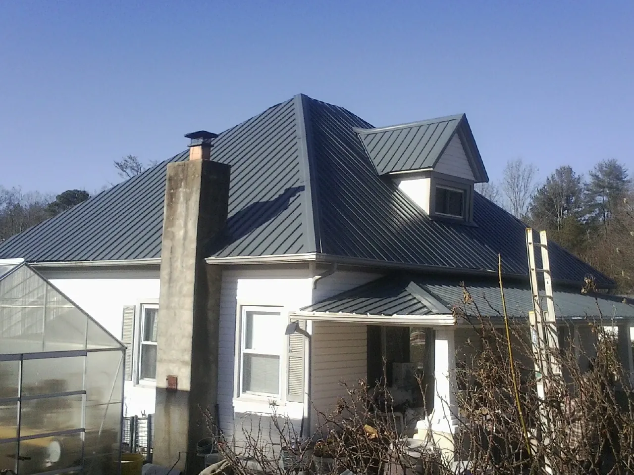 Dark blue standing seam metal roof on a white farmhouse with dormer — Slate & Tile Roof Repair by Roofing Brothers in Tribune