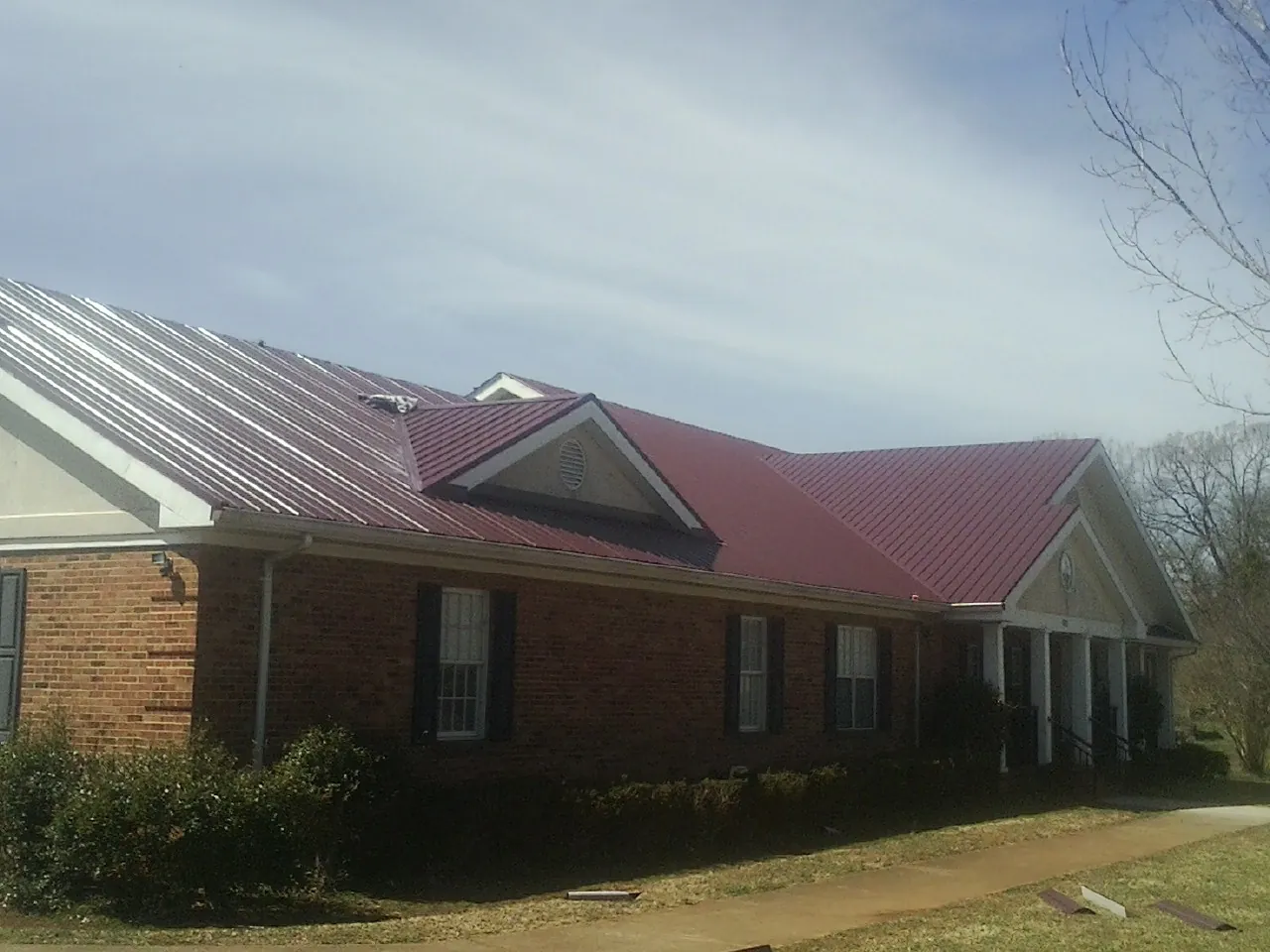 Red metal roof with gabled entries on a long brick building, from a Hail Damage Roof Repair job in Tribune