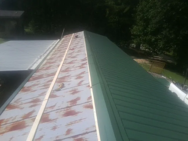 Old rusted panels beside newly installed green metal roofing — Wind Damage Roof Repair by Roofing Brothers in Tribune