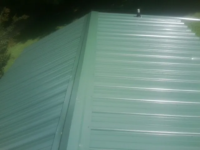 New green metal panels meeting at the ridge of a roof — Flat Roof Repair work by our crew in Tribune