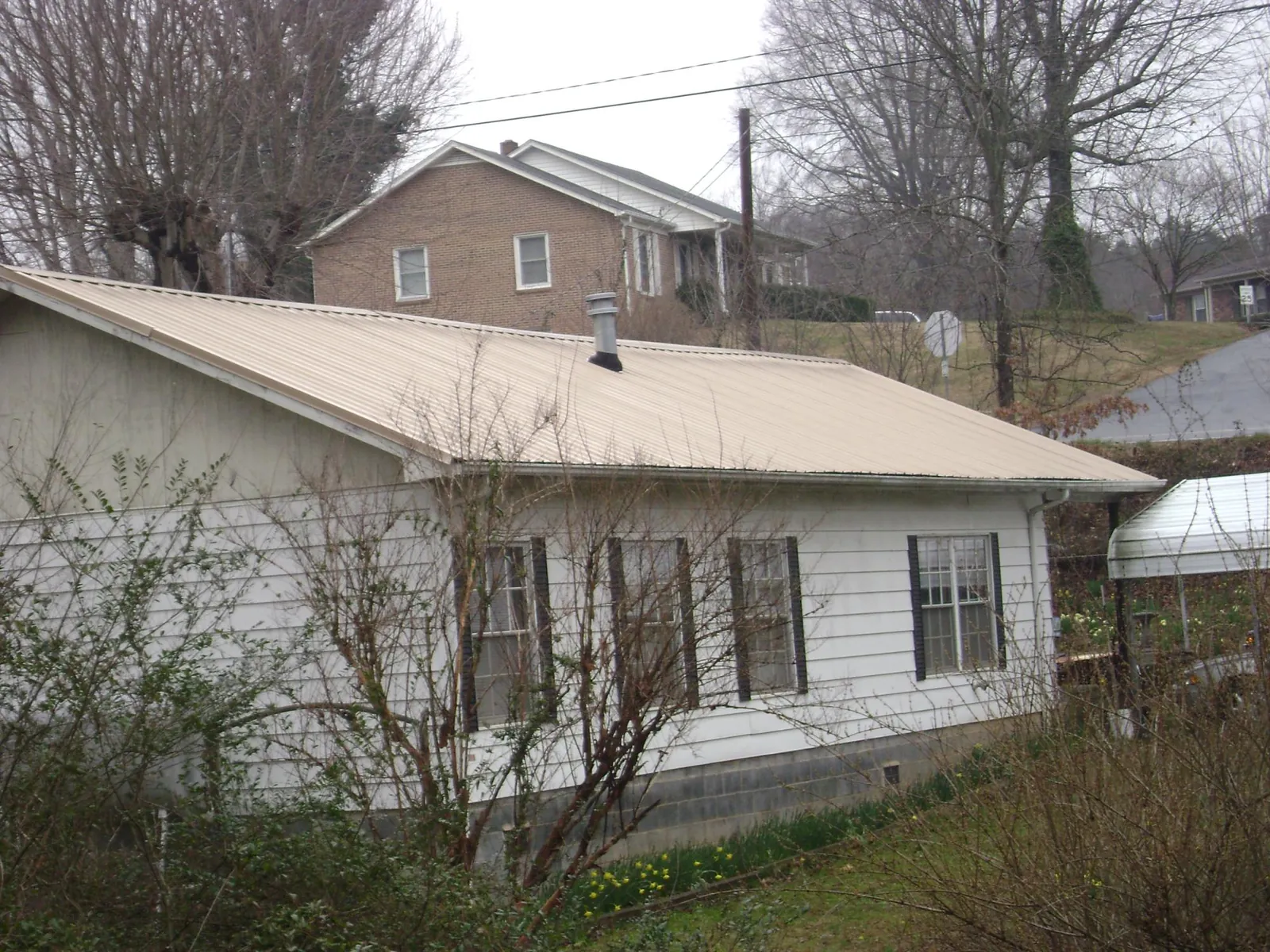 Tan metal roof on a white sided house set into a hillside in Tribune