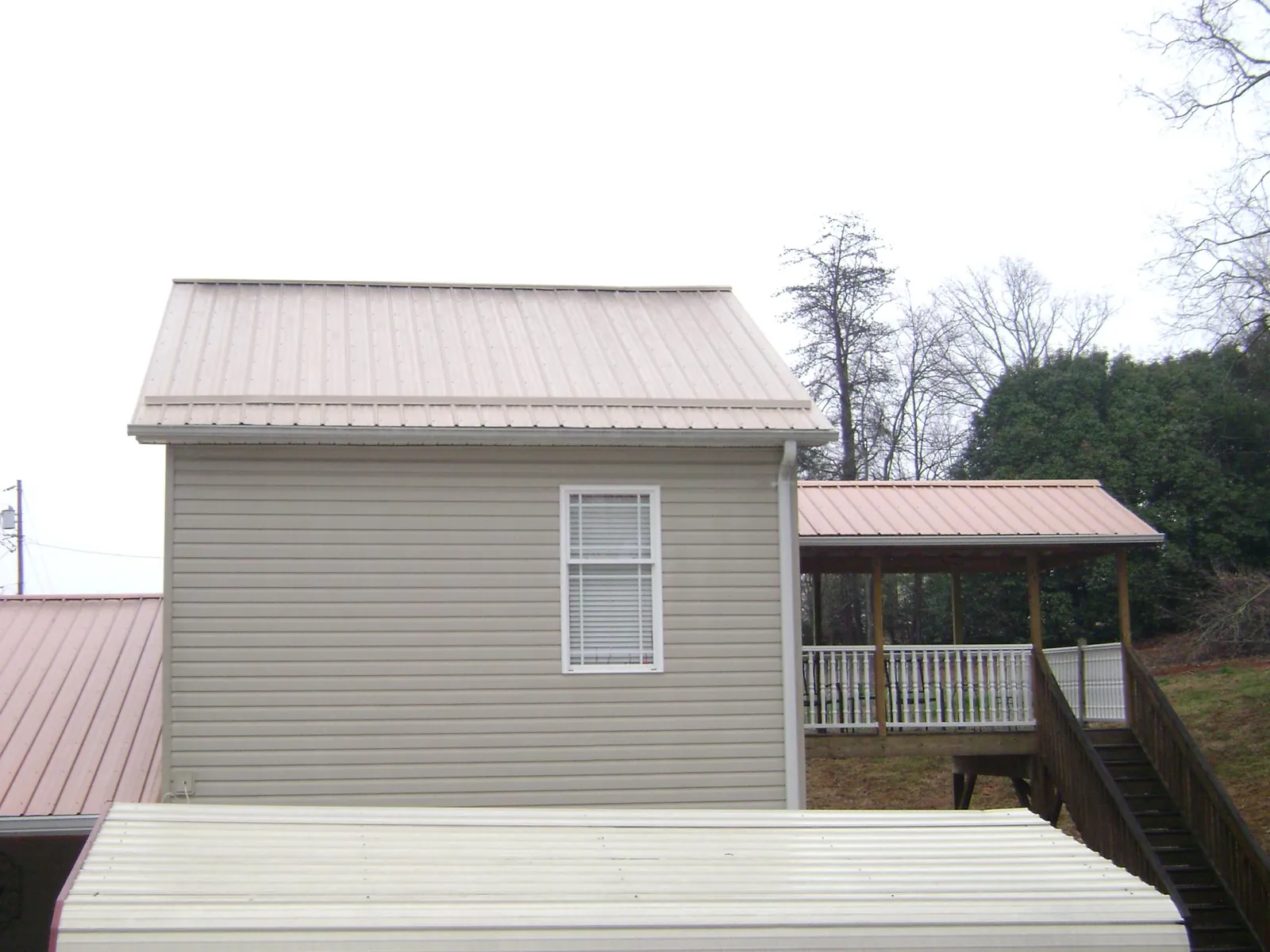 Tan metal roofs on a two story addition and attached porch, from a Roof Replacement job in Tribune